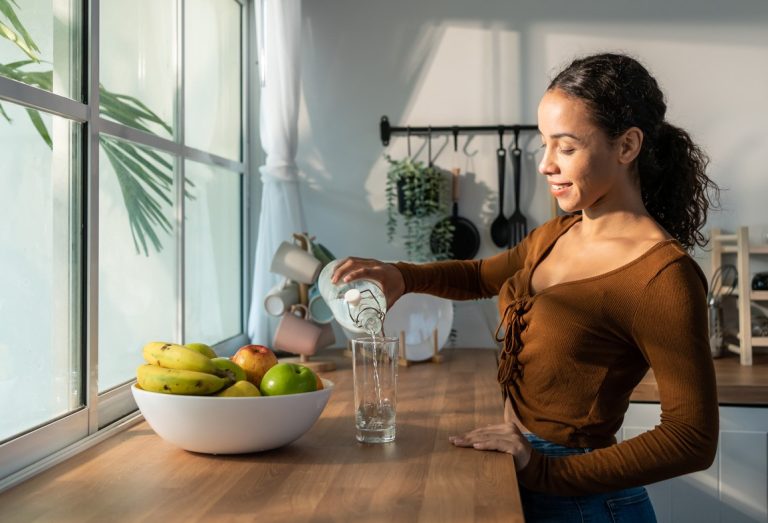 femme en train de servir un verre d’eau dans une cuisine avec une corbeille de fruits